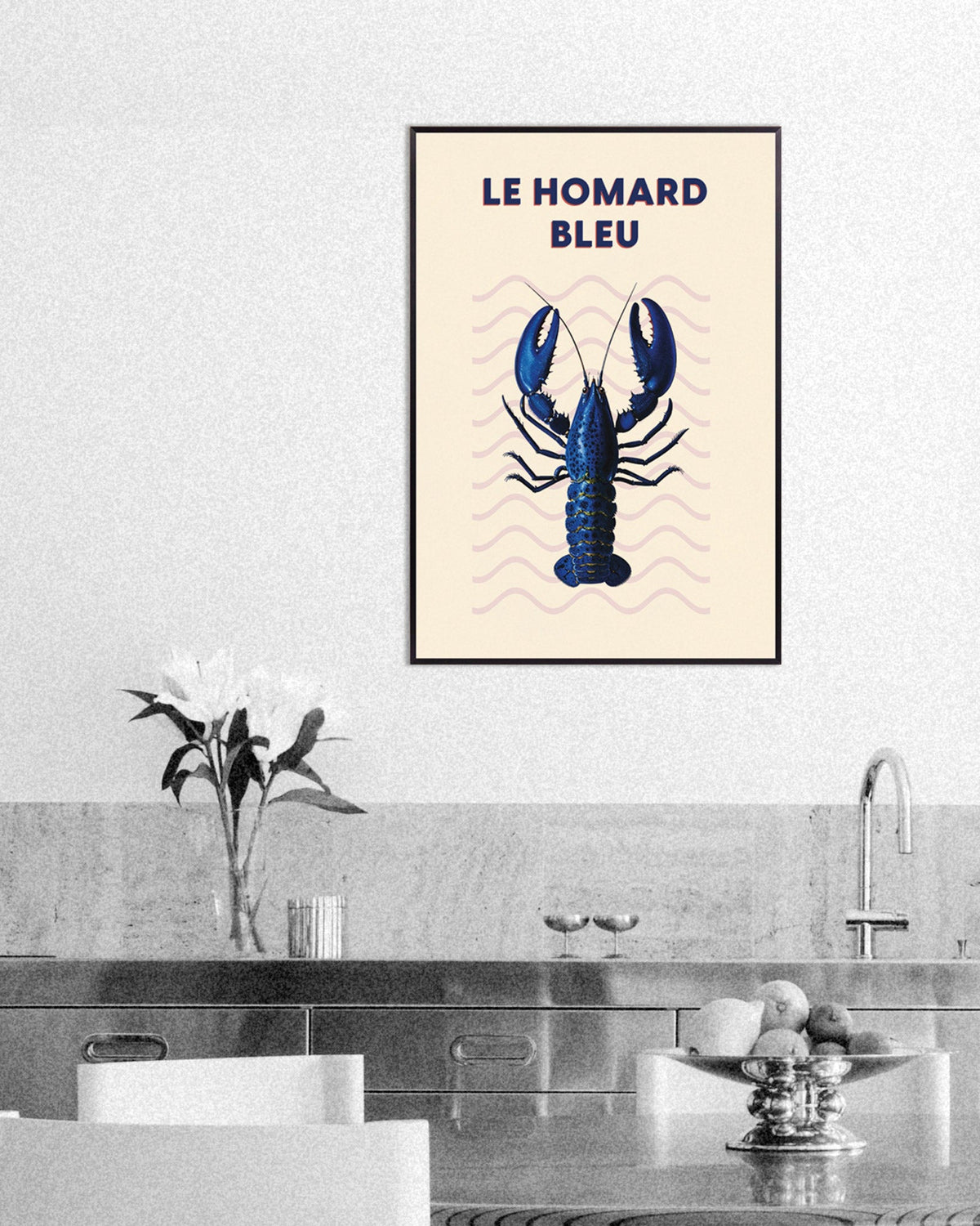 Kitchen with a framed poster of a blue lobster titled Le Homard Bleu above a steel counter with flowers and a fruit bowl